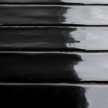 Glossy black rectangular tiles lie in parallel rows, reflecting a cloudy sky above, creating a sleek, modern appearance.