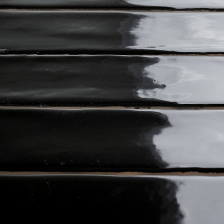 Glossy black rectangular tiles lie in parallel rows, reflecting a cloudy sky above, creating a sleek, modern appearance.