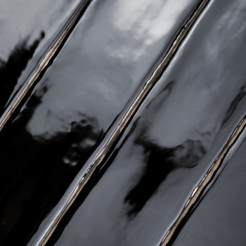 Glossy black tiles reflect light, creating a wavy, mirrored effect. The surface appears wet, highlighting elongated rectangular 