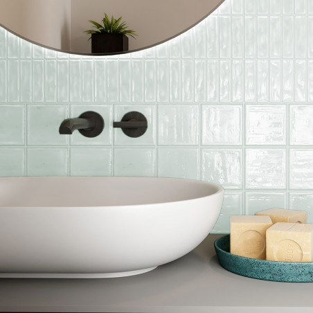 A white ceramic sink rests against glossy light green tile wall, accompanied by a teal dish holding square soap bars, in a bathr