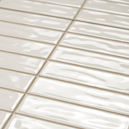 Les carreaux rectangulaires beige brillant sont disposés en quinconce. La surface présente des textures ondulées, réfléchissant 