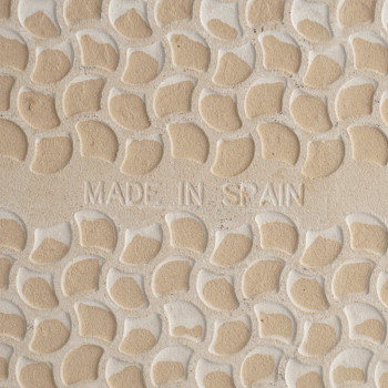 De tegel heeft een patroon van verhoogde, gebogen beige vormen met lichte voeglijnen, met in het midden de tekst `MADE IN SPAIN`