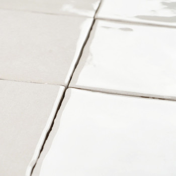White square tiles with reflective surfaces lie flat, aligned in a grid pattern. The grout between them is slightly uneven.