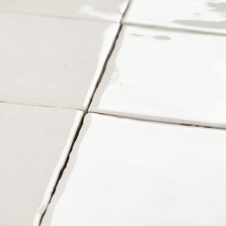 White square tiles with reflective surfaces lie flat, aligned in a grid pattern. The grout between them is slightly uneven.