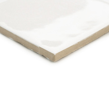 Un azulejo de cerámica blanca con un acabado brillante se encuentra en ángulo y muestra un borde beige sin esmaltar, lo que sugi