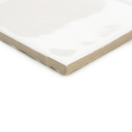 Un azulejo de cerámica blanca con un acabado brillante se encuentra en ángulo y muestra un borde beige sin esmaltar, lo que sugi