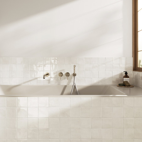 Los azulejos de cerámica blancos forman un fondo limpio y brillante en un baño. Un grifo de bañera está montado en el centro con