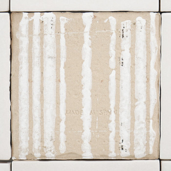 Un azulejo de cerámica beige, con vetas blancas verticales, se coloca en el centro entre azulejos blancas más pequeñas. El texto