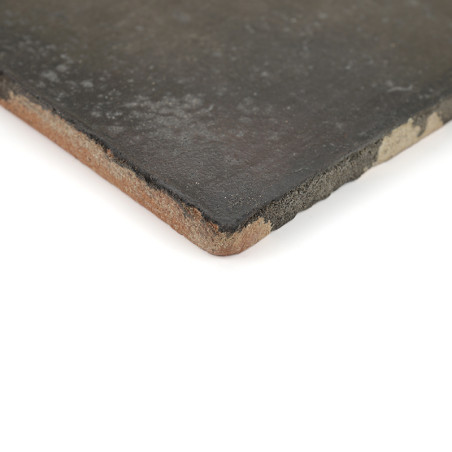 A terracotta tile with dark, smooth surface lies flat, displaying chipped edges, against a plain white background.