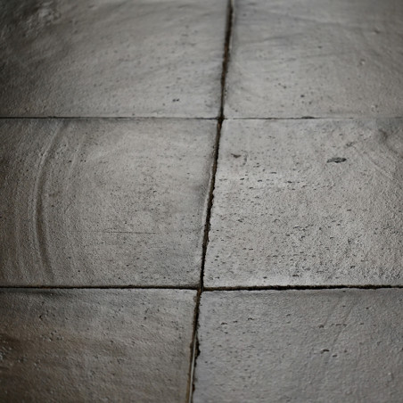 Square terracotta tiles lie adjacent, subtly textured with circular patterns, forming a weathered floor in dim lighting.