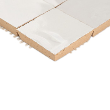 A white glazed terracotta tile resting on a plain white surface, showcasing texture and square shape with visible edges.