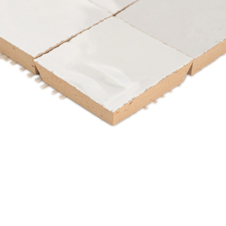 A white glazed terracotta tile resting on a plain white surface, showcasing texture and square shape with visible edges.