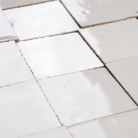 White glazed terracotta tiles are arranged neatly in a grid pattern, reflecting light in a bright, minimalistic setting.