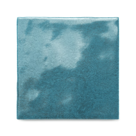 Un carreau de céramique carré scintille avec un vernis bleu sarcelle brillant, reflétant de subtiles variations de lumière, sur 