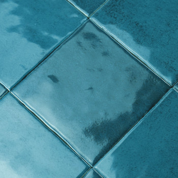 Les carreaux de céramique, émaillés dans des tons de bleu, reflètent la lumière dans une gamme d'éclats brillants, disposés en f
