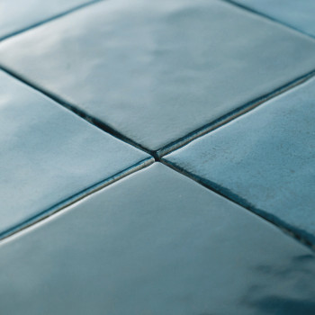Quatre carreaux bleus lisses et brillants sont joints aux coins, créant un motif de grille. La surface est réfléchissante, avec 