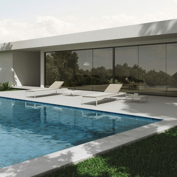 Une piscine élégante aux eaux bleues carrelées, flanquée de chaises longues blanches, reflète une maison moderne avec de grandes