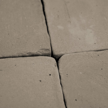 Quatre carreaux de terre cuite, rapprochés, forment un motif carré. la surface présente une texture inégale et rustique et des i