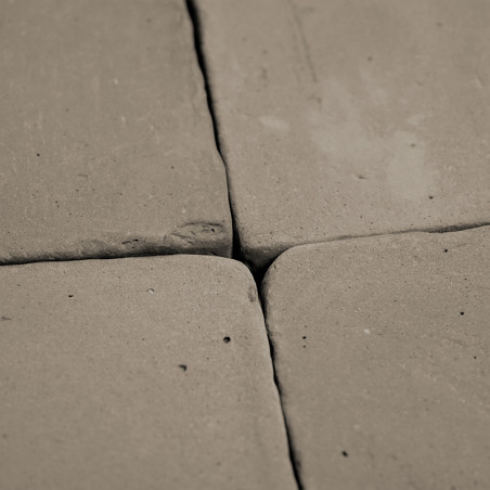 Quatre carreaux de terre cuite, rapprochés, forment un motif carré. la surface présente une texture inégale et rustique et des i