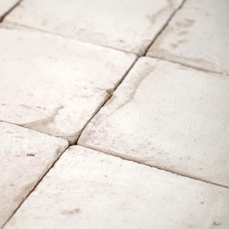 White terracotta tiles, arranged in a grid, display natural texture variations and subtle stains, forming a rustic floor pattern