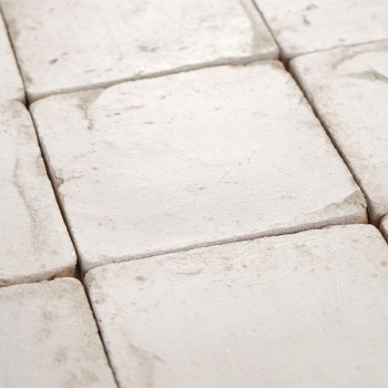 Square terracotta tiles rest in a neat grid pattern, displaying a smooth, weathered texture in soft, natural light.