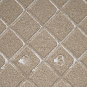 Un carreau beige texturé avec un motif en losange en relief affiche « MADE IN SPAIN » au centre, entouré de subtiles marques de 