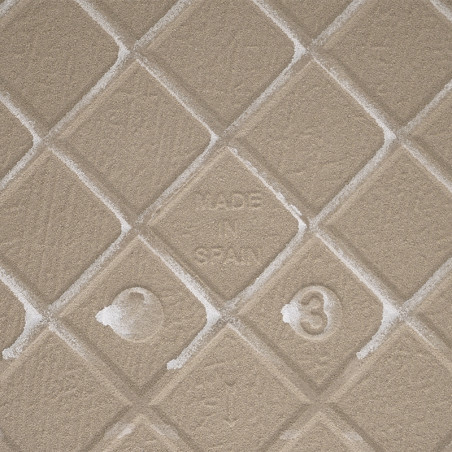 Un carreau beige texturé avec un motif en losange en relief affiche « MADE IN SPAIN » au centre, entouré de subtiles marques de 