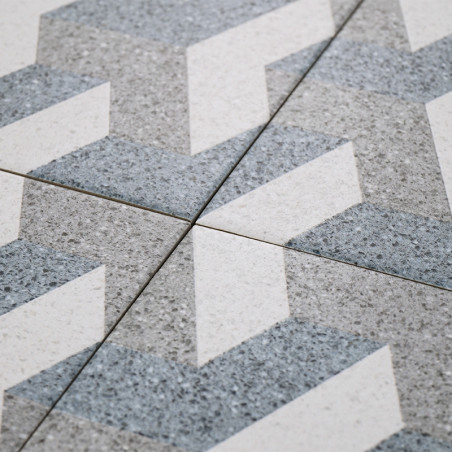 Les carreaux gris et blancs forment un motif en zigzag, se croisant au niveau des lignes de coulis, créant un motif géométrique 