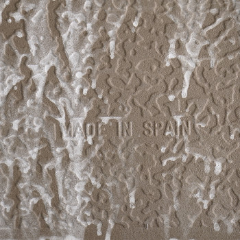 Braune Fliese mit strukturierten weißen Mustern, die an abstrakte Wellen erinnern. In der Mitte ist der Text „MADE IN SPAIN“ ein