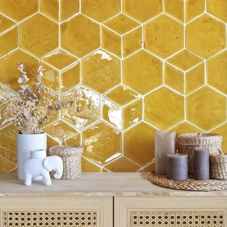 Des carreaux hexagonaux en terre cuite jaune forment un mur texturé au-dessus d'une table en bois avec des bougies et des objets