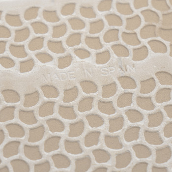 Azulejo texturizado com padrão de favo de mel em relevo, exibindo o texto `MADE IN SPAIN.` A superfície tem um fundo bege.
