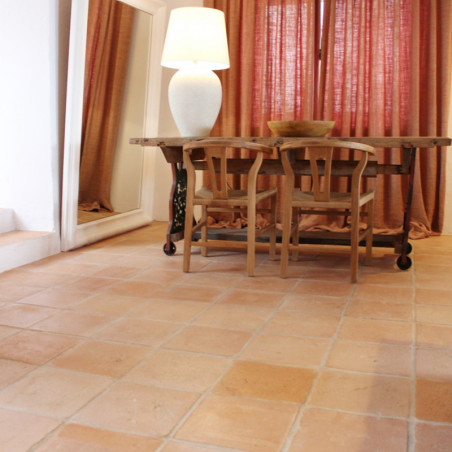 Los azulejos de terracota forman un suelo rústico, soportando muebles de madera y una lámpara en una habitación cálidamente ilum