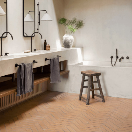 Les carreaux de terre cuite forment un motif à chevrons sur le sol d'une salle de bain, avec un tabouret en bois et une décorati
