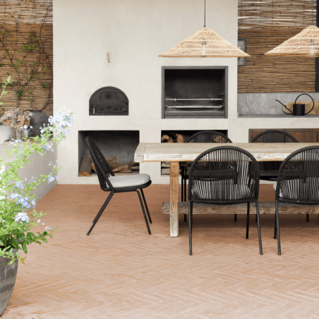 Des carreaux de terre cuite recouvrent un patio abritant un ensemble de salle à manger en bois, sous des lampes en paille, avec 