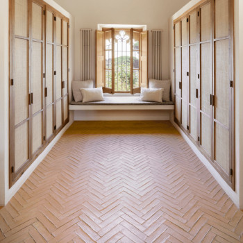 Le sol en carrelage en terre cuite disposé en chevrons, flanqué d'armoires en bois, mène à un banc de fenêtre ensoleillé.