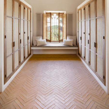 Le sol en carrelage en terre cuite disposé en chevrons, flanqué d'armoires en bois, mène à un banc de fenêtre ensoleillé.