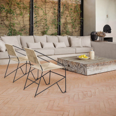 Le sol en carrelage en terre cuite supporte des chaises en métal noir et une table en pierre, dans un espace de vie confortable 