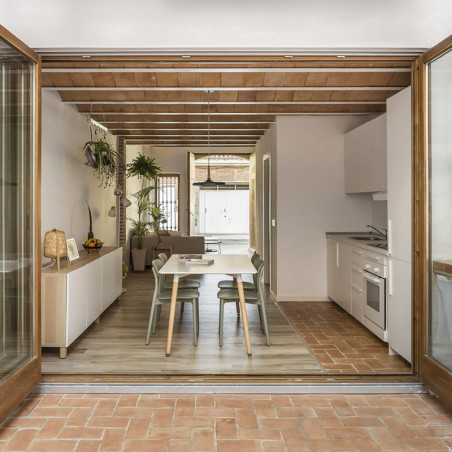 Les carreaux de terre cuite forment un chemin menant à une cuisine-salle à manger moderne, entourée de meubles en bois et blancs
