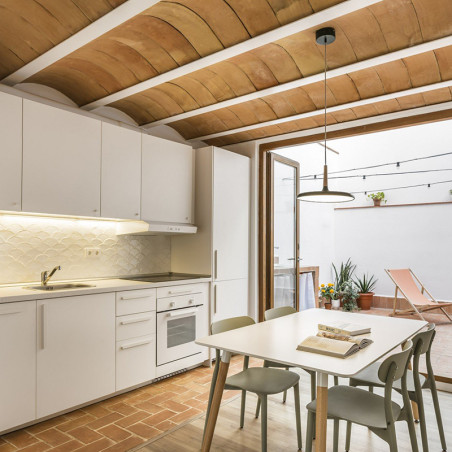 Terracotta tiles form arched ceiling above a modern kitchen with white cabinets, dining table, and adjacent patio seating area.