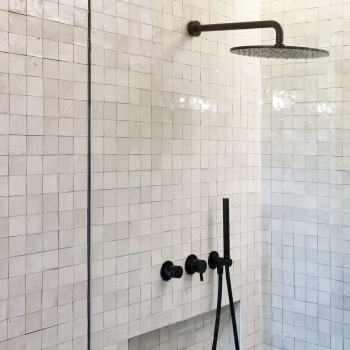 Showerhead protrudes from the wall, surrounded by glossy, square, white terracotta tiles in a modern, minimalist bathroom.