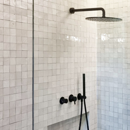 Showerhead protrudes from the wall, surrounded by glossy, square, white terracotta tiles in a modern, minimalist bathroom.