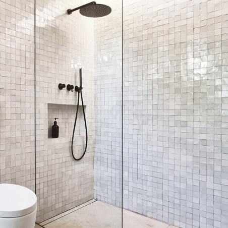 White terracotta tiles line a modern shower area, featuring a black rain shower head and handle, with glass enclosure.