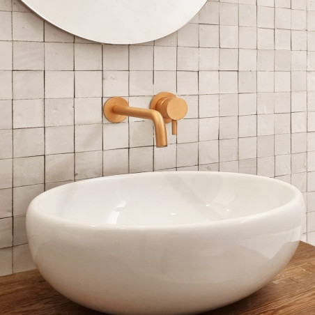 A white oval sink sits beneath a gold faucet, against a white square-tiled wall, creating a modern bathroom aesthetic.