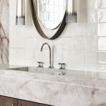 Los azulejos de terracota blanca se alinean en la pared del baño y reflejan la luz alrededor de una encimera de mármol con un gr