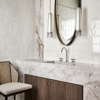 Los azulejos de terracota blanca cubren la pared del baño y reflejan la luz. lavabo de mármol debajo, flanqueado por espejos y l