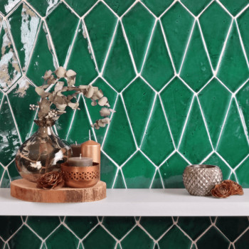 Des carreaux de terre cuite verte forment un motif géométrique. des vases décoratifs et des bougies reposent sur une étagère bla