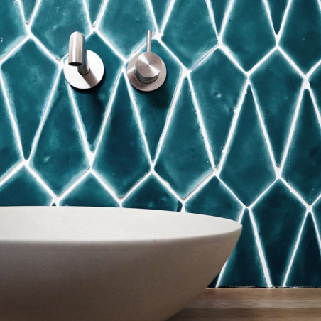 Blue geometric terracotta tiles cover a bathroom wall above a modern white vessel sink, with two metal faucets mounted.