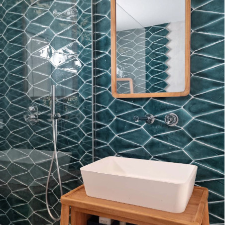 A rectangular white basin sits on a wooden stand, adjacent to glossy green geometric tiles in a bathroom setting.