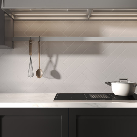 Een witte pot staat op een strak fornuis onder een rij hangend keukengerei in een moderne keuken met tegels met visgraatmotief.