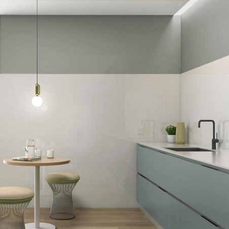Een moderne keuken is voorzien van strakke, matte saliegroene kasten langs de muur. Een ronde tafel met twee krukken staat onder